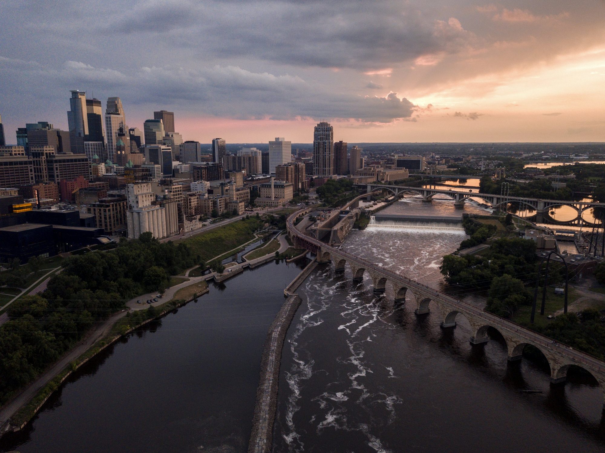 The Stone Arch Bridge curving across the Mississippi at Saint Anthony Falls, with the Minneapolis skyline at dusk